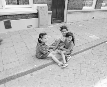 885027 Afbeelding van drie meisjes van niet-Nederlandse afkomst zittend op een stoeprand in de Riouwstraat te Utrecht.